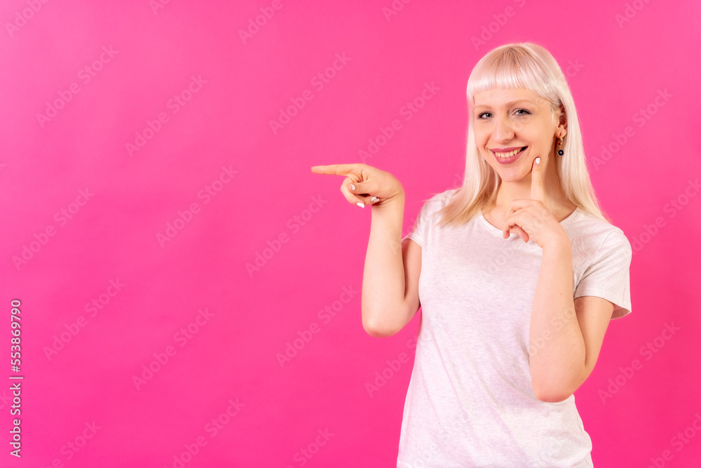 Blonde caucasian girl studio shot on pink background, copy space, smiling pointing left Blonde caucasian girl studio shot on pink background, copy space, smiling pointing left