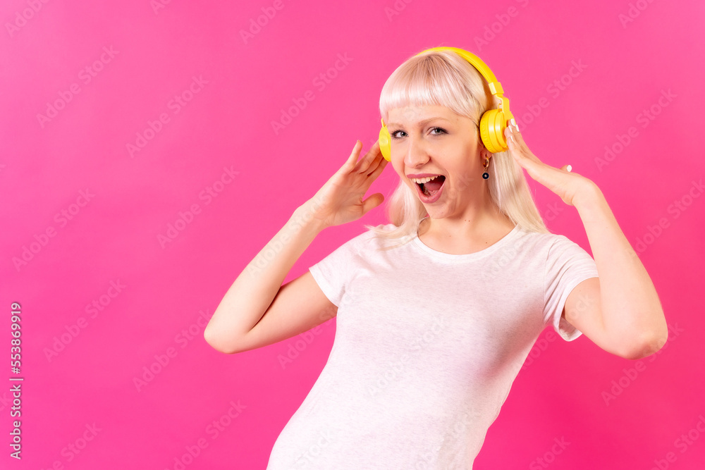 Blonde caucasian girl in studio on pink background, smiling listening to music with headphones Blonde caucasian girl in studio on pink background, smiling listening to music with headphones