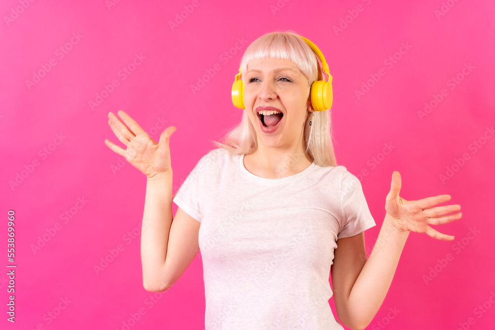 Blonde caucasian girl in studio on pink background, dancing listening to music with headphones Blonde caucasian girl in studio on pink background, dancing listening to music with headphones