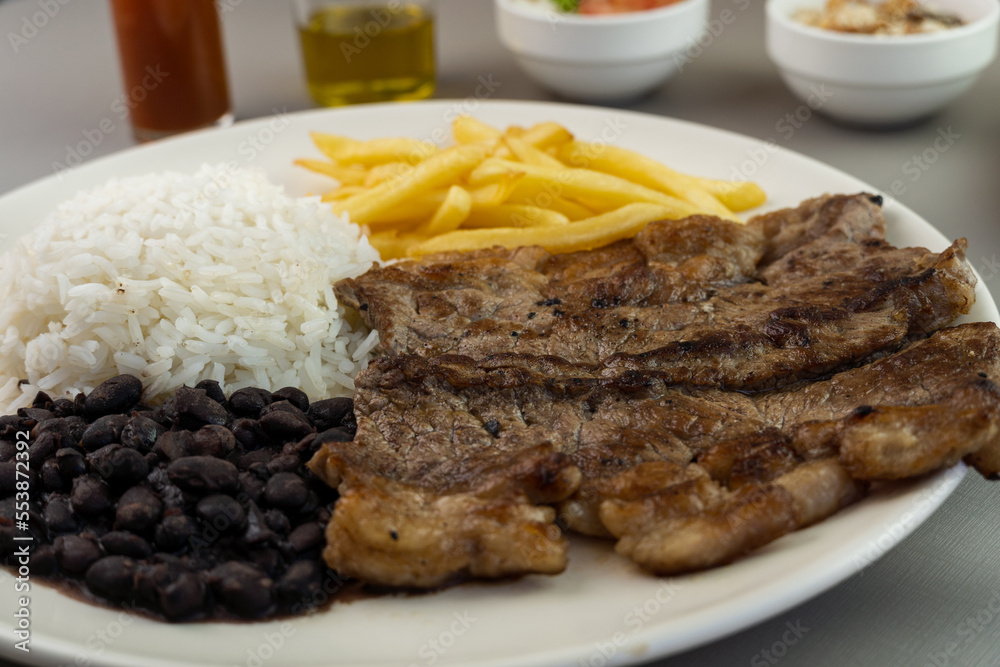 Delicious executive dish of beef steak, rice, beans, french fries and green salad with lettuce, tomato and onion accompanied by farofa and vinaigrette. Typical Brazilian food. Selective focus Delicious executive dish of beef steak, rice, beans, french fries and green salad with lettuce, tomato and onion accompanied by farofa and vinaigrette. Typical Brazilian food. Selective focus