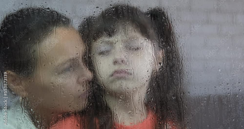 Upset time by mother. A pensive mother embrace her daughter by the wet rainy window in the room.