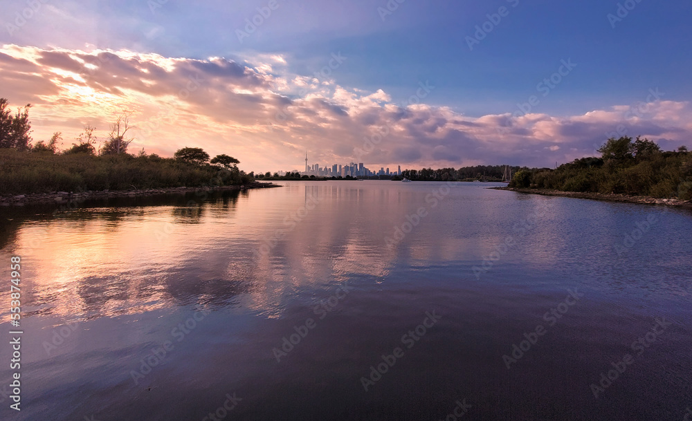Autumn view from Tommy Thompson Park across bays of Lake Ontario with Toronto skyline and magnificent sunset skies with pink clouds and their reflection in rippled surface of the lake