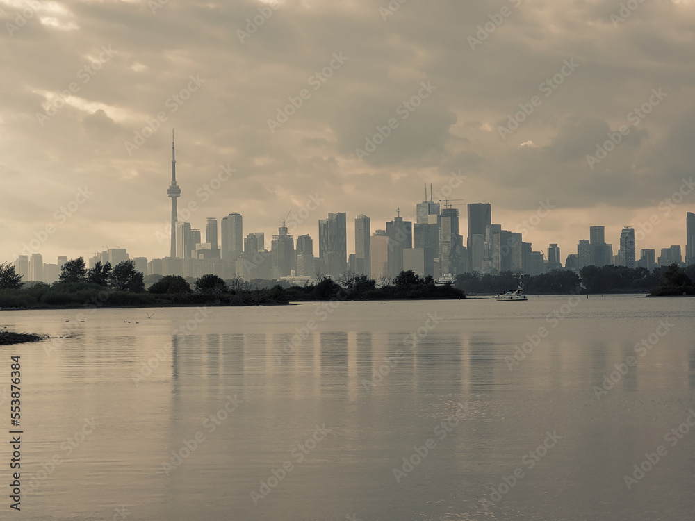 Autumn day view across inner bays of Lake Ontario in Tommy Thompson Park with foggy Downtown Toronto skyline under grey cloudy skies in background with water surface reflecting the buildings outlines
