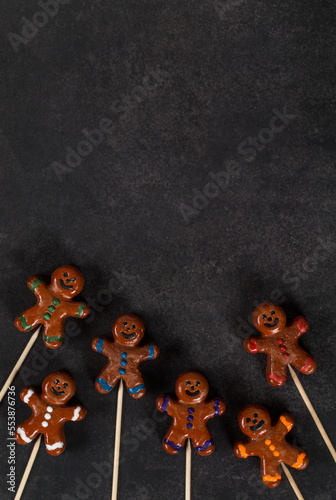 Christmas dessert in the form of a gingerbread man, covered with chocolate and colored icing sugar, on a wooden stick. Dark gray background. Top view. Copy space