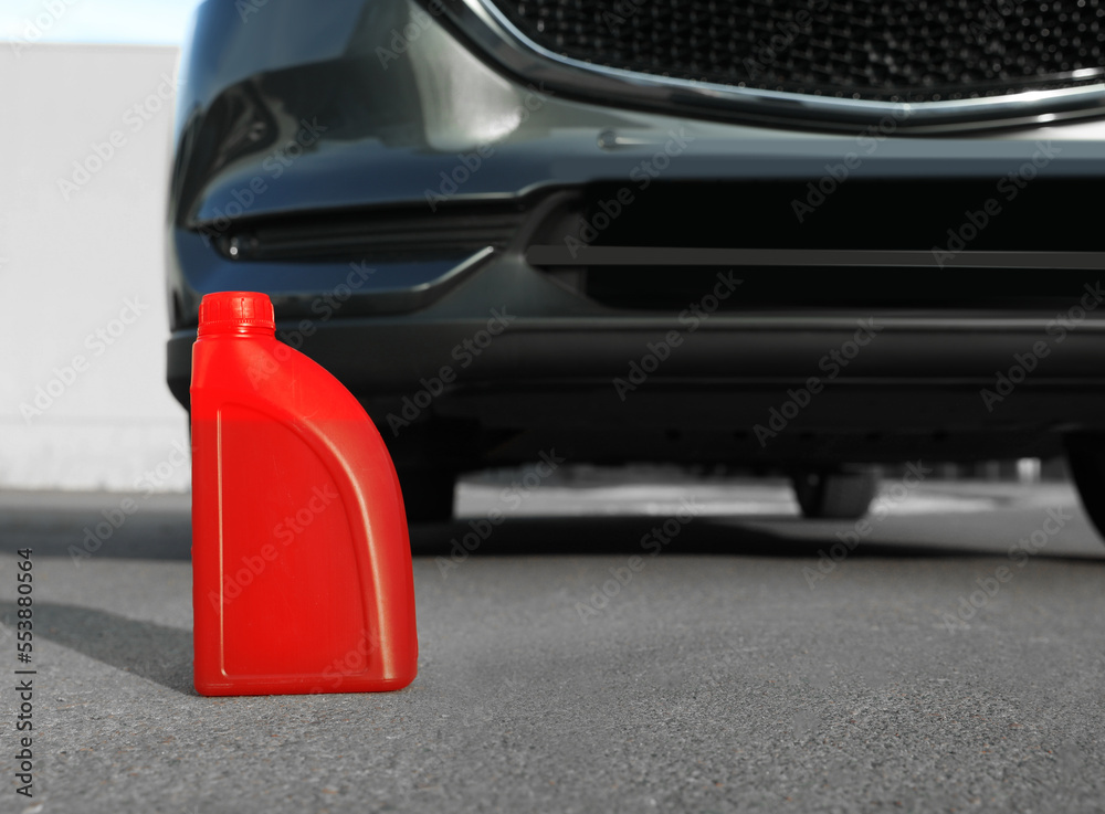 Red canister with motor oil near car on asphalt road Red canister with motor oil near car on asphalt road