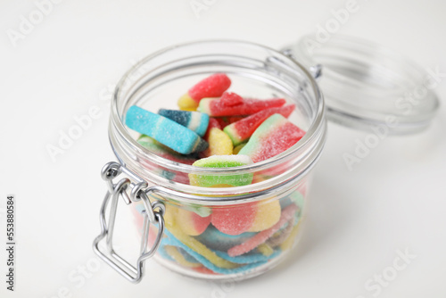 Tasty jelly candies in open jar on white table, closeup