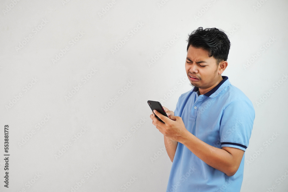 sad face with holding phone young asian man wearing blue polo t shirt isolated on white background. irritated face expressions sad face with holding phone young asian man wearing blue polo t shirt isolated on white background. irritated face expressions