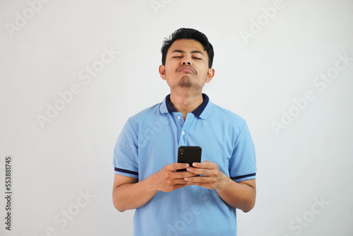 sad face with holding phone young asian man wearing blue polo t shirt isolated on white background. irritated face expressions © DMH