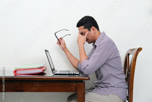Side view of Asian man sitting in front of laptop showing stress gesture photo