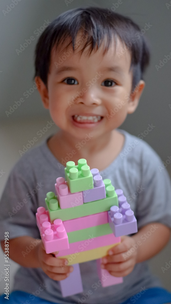 Happy child, cute asian toddler boy building house from plastic blocks sitting at floor. Happy child, cute asian toddler boy building house from plastic blocks sitting at floor.