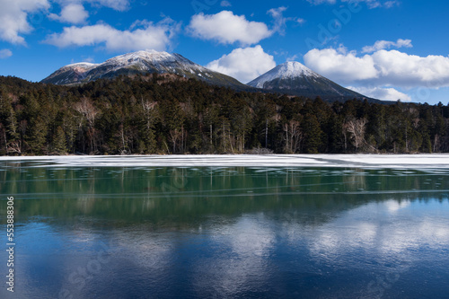 水面が凍った冬の湖及び頂上に雪を被った山々。日本の北海道のオンネトー湖。