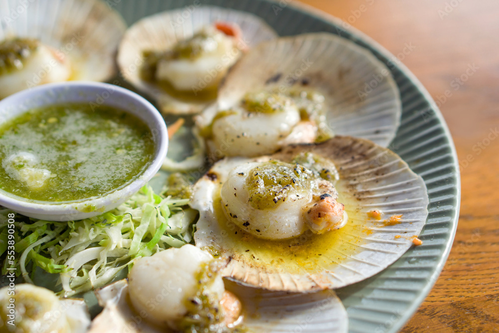 Closeup scallops butter and garlic sauce on ceramic plate served with spicy sauce on wooden table.