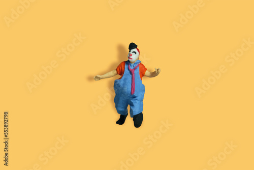 Miniature people toy figure photography. Full body of a clown wearing tie and jumper suit. Isolate on orange background