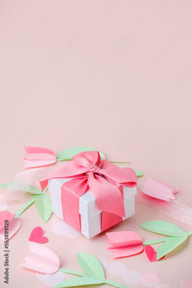 Holiday pink background with gift, luxury pink satin bow, ribbon, paper cut flowers. Valentine's Day, Happy Women's Day, Mother's Day, Birthday, Wedding. Space for text, stylish flyer, greeting card