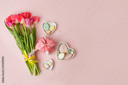 Happy Easter. Multi-colored pastel easter cookies gingerbread, gift box seasonal flowers tulips on pink background. Easter concept, copy space, flyer, banner, coupon, greeting card, invitation