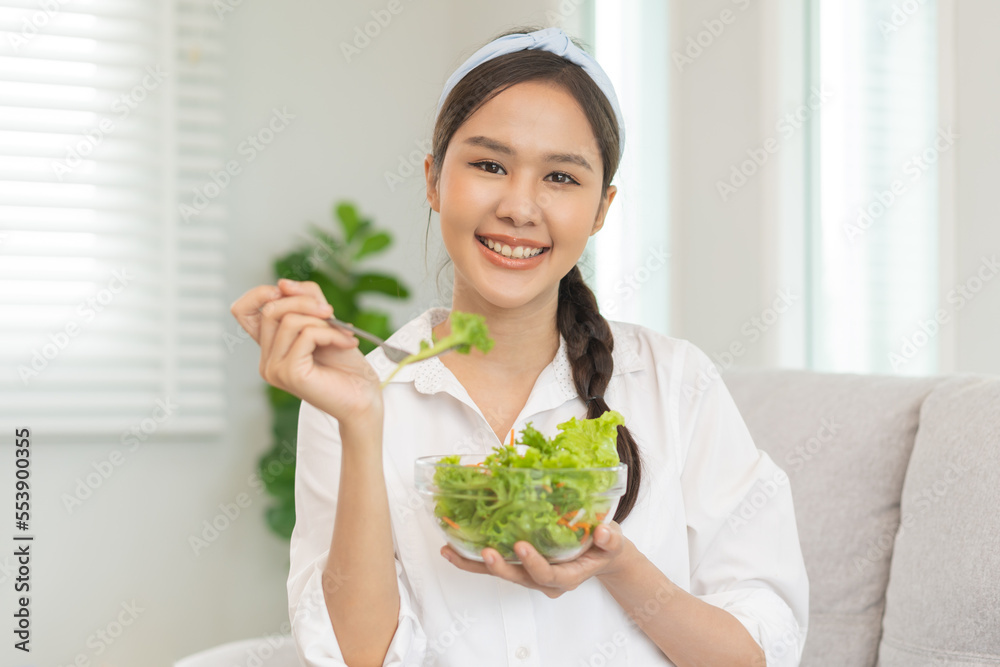 Diet, Dieting asian young woman, girl hand use fork at lettuce on mix vegetables, green salad bowl, eat food low fat to good body sitting on sofa at home. Nutritionist female, Weight loss for healthy. Diet, Dieting asian young woman, girl hand use fork at lettuce on mix vegetables, green salad bowl, eat food low fat to good body sitting on sofa at home. Nutritionist female, Weight loss for healthy.