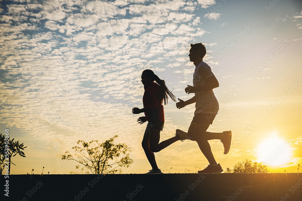 Silhouette of young couple running together on road. Couple, fit runners fitness runners during outdoor workout with sunset background.