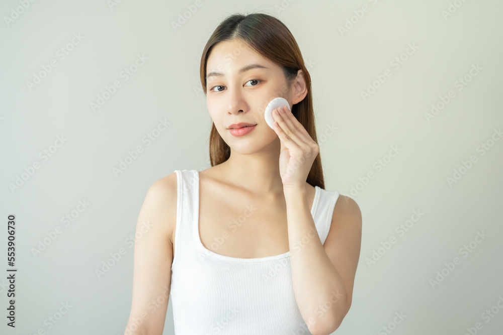 Happy beauty, attractive asian young woman, girl looking camera hand holding cotton pad, applying facial wipe on her face remover makeup, essence or lotion of skin care. Isolated on white background. Happy beauty, attractive asian young woman, girl looking camera hand holding cotton pad, applying facial wipe on her face remover makeup, essence or lotion of skin care. Isolated on white background.