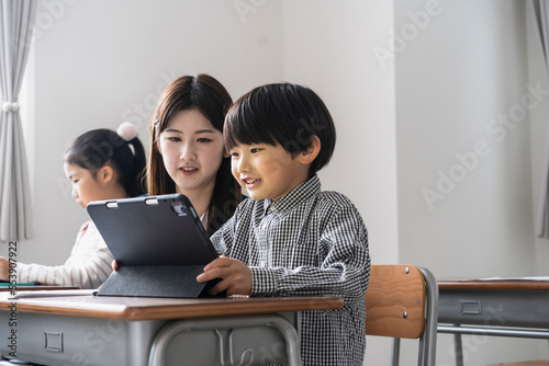 タブレットPCを使った授業をする日本人小学生の男の子と女性教師