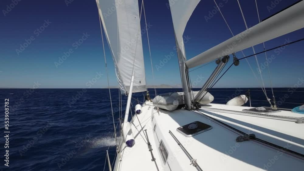 Floating sailing yacht with spread sails splitting the sea waves and an island on the horizon. Sail yacht floats by the storming sea. Bow of the boat cutting through the sea. Summer vacation shots. Floating sailing yacht with spread sails splitting the sea waves and an island on the horizon. Sail yacht floats by the storming sea. Bow of the boat cutting through the sea. Summer vacation shots.