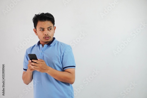 expression of dislike trying to dodge with holding phone young asian man wearing blue polo t shirt isolated on white background