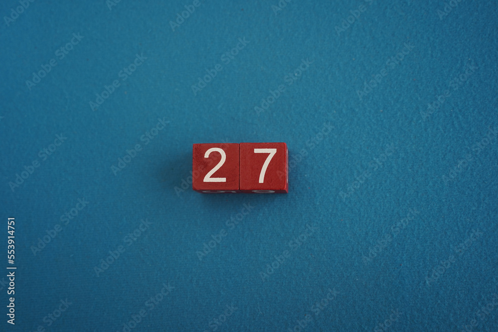 Wooden Viva Magenta cubes with number 27 blue background close-up top view. Concept of date or time. White numbers 27 on red cubes velvet background. Copy space for text or event. Blurred background Wooden Viva Magenta cubes with number 27 blue background close-up top view. Concept of date or time. White numbers 27 on red cubes velvet background. Copy space for text or event. Blurred background