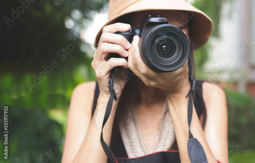 Asian woman wearing hat and sleeveless top  taking photos in the park with dslr camera.  selective focus on lens © Phuttharak