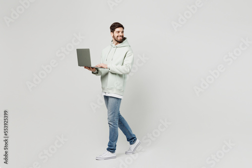 Full body young fun caucasian man wear mint hoody look camera hold use work on laptop pc computer look aside on area isolated on plain solid white background studio portrait. People lifestyle concept.
