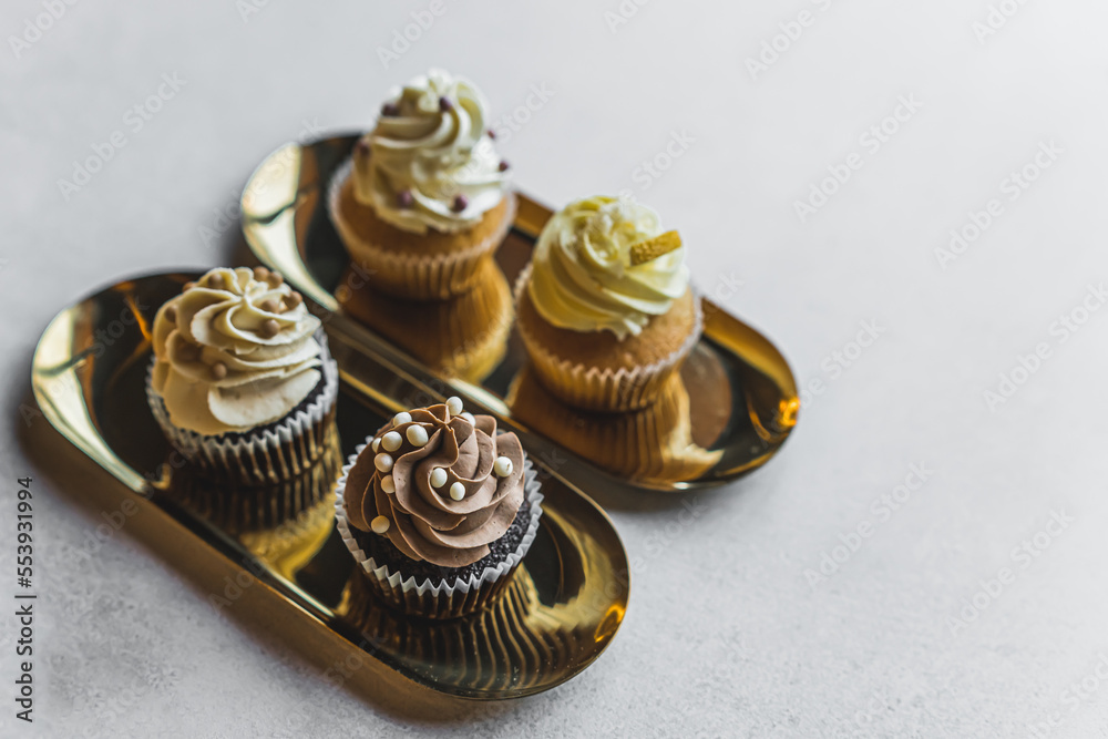 Four various frosted cupcakes with sprinkles arranged on small golden platters on white table. Fancy baked goods. Baking. Horizontal shot . High quality photo Four various frosted cupcakes with sprinkles arranged on small golden platters on white table. Fancy baked goods. Baking. Horizontal shot . High quality photo