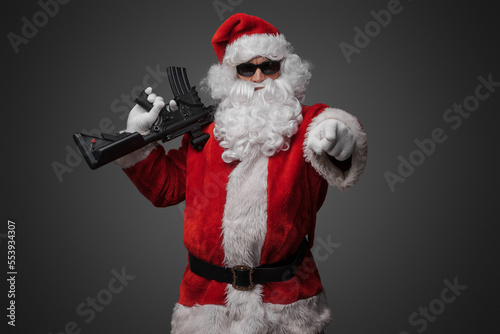 Shot of cool santa holding rifle on his shoulder pointing his finger at camera.