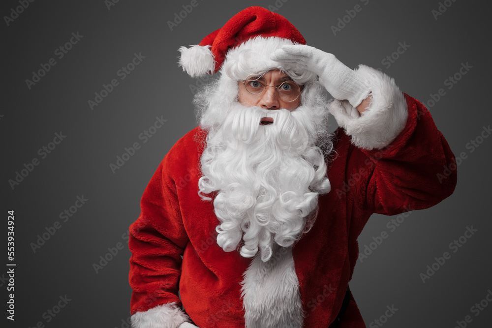Portrait of old santa claus dressed in red suit with his hand at his forehead.