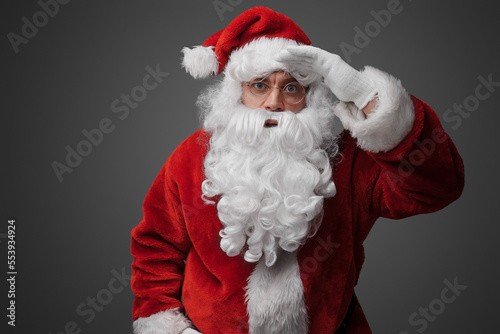 Portrait of old santa claus dressed in red suit with his hand at his forehead.