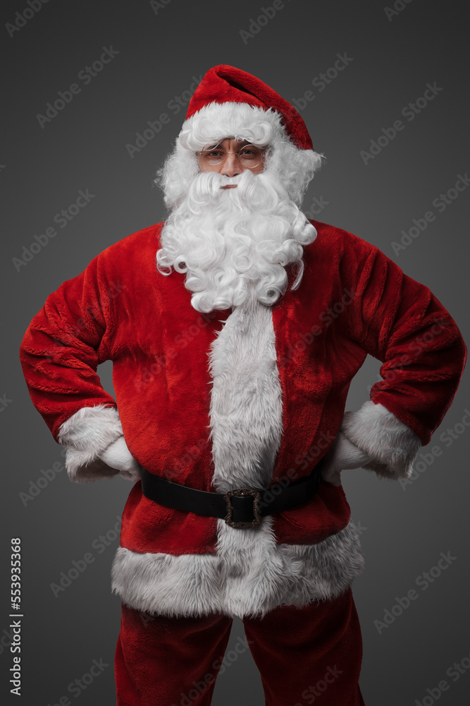 Portrait of isolated on grey santa dressed in red costume staring at camera.