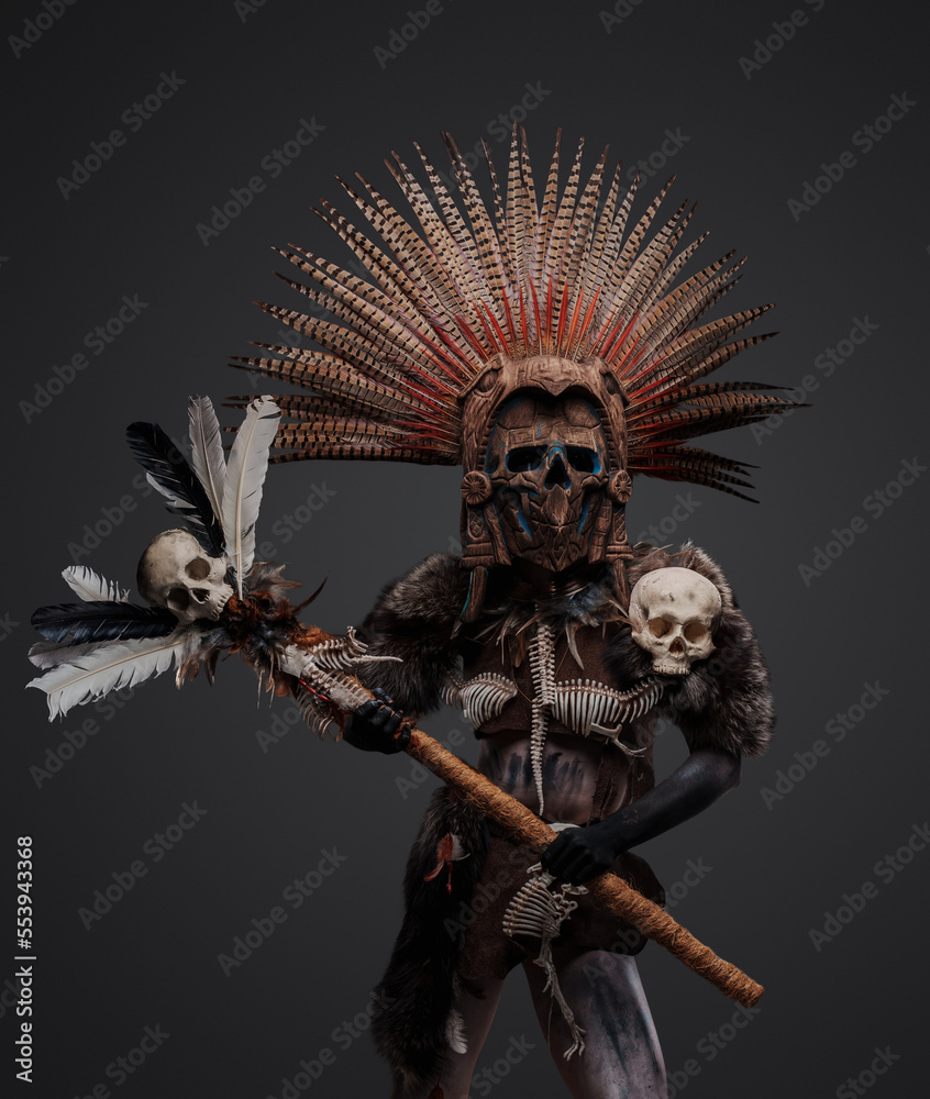 Photo of aztec witch from past with plumed headdress and mask holding staff with skull head. Photo of aztec witch from past with plumed headdress and mask holding staff with skull head.