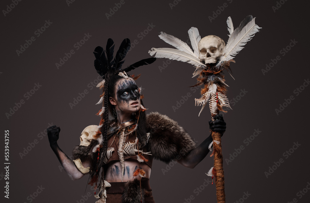 Shot of painted dark witch with fur and staff against grey background. Shot of painted dark witch with fur and staff against grey background.