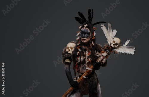 Shot of dark witch woman with fur holding staff against grey background.