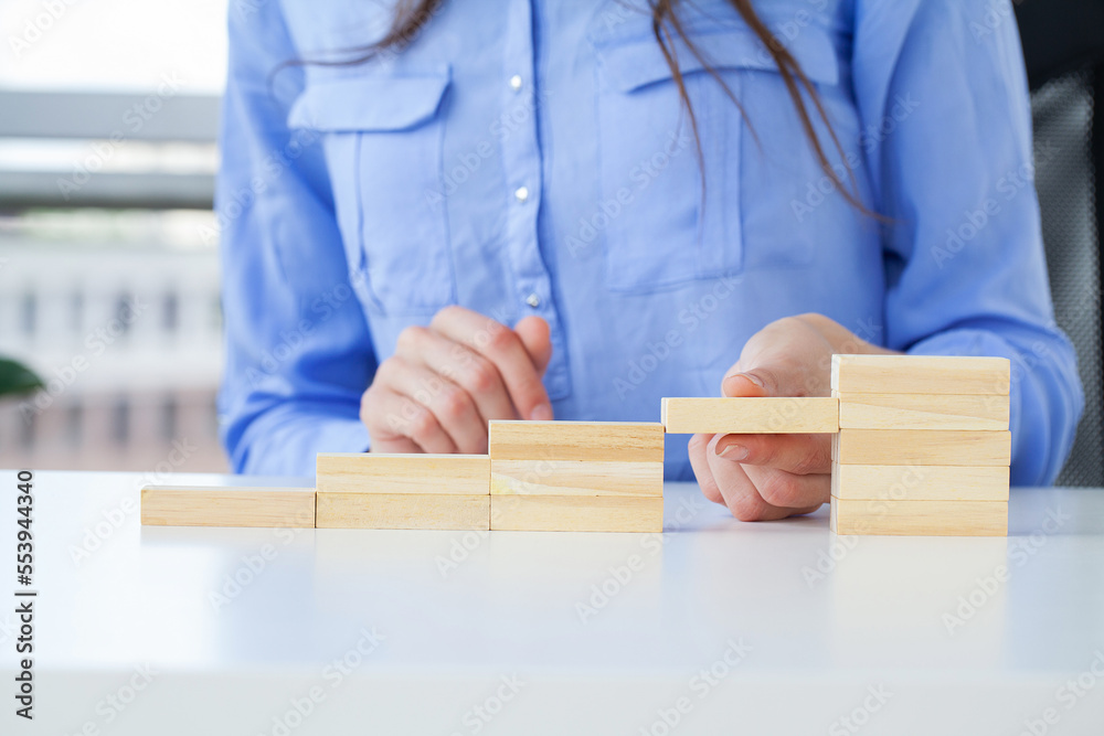 Woman hand arranging wood cube stacking as stair step shape