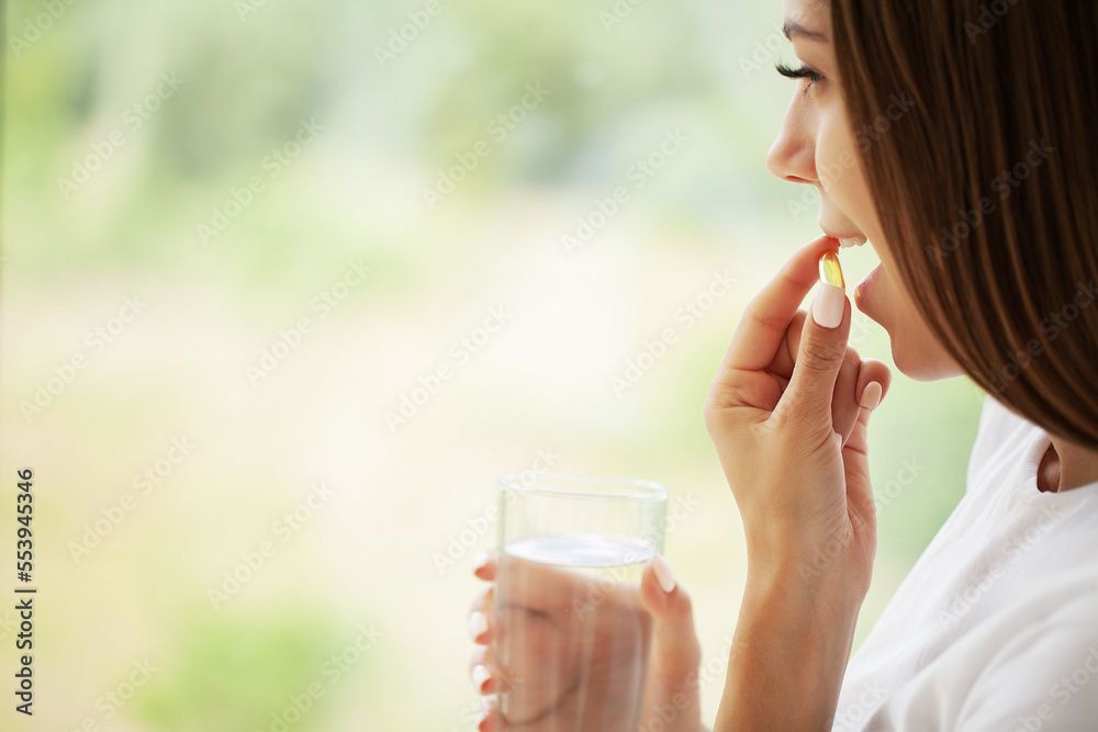 Φωτογραφία Young woman takes round pill with glass of water in hand