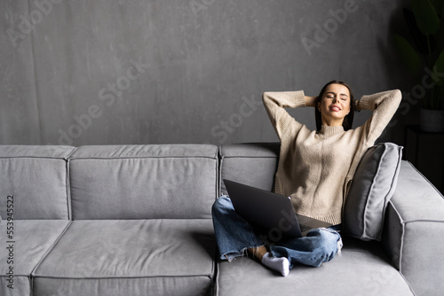 Happy woman using laptop sitting on cosy sofa