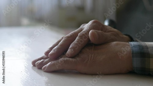 close-up of the wrinkled hands of an elderly man and a walking stick, selective focus. vile people, a pensive pensioner sits with his hands folded on the table. real people, old age and loneliness