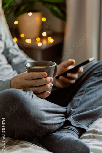 a caucasian man relaxing at home  drinking coffee and using smartphone in bed