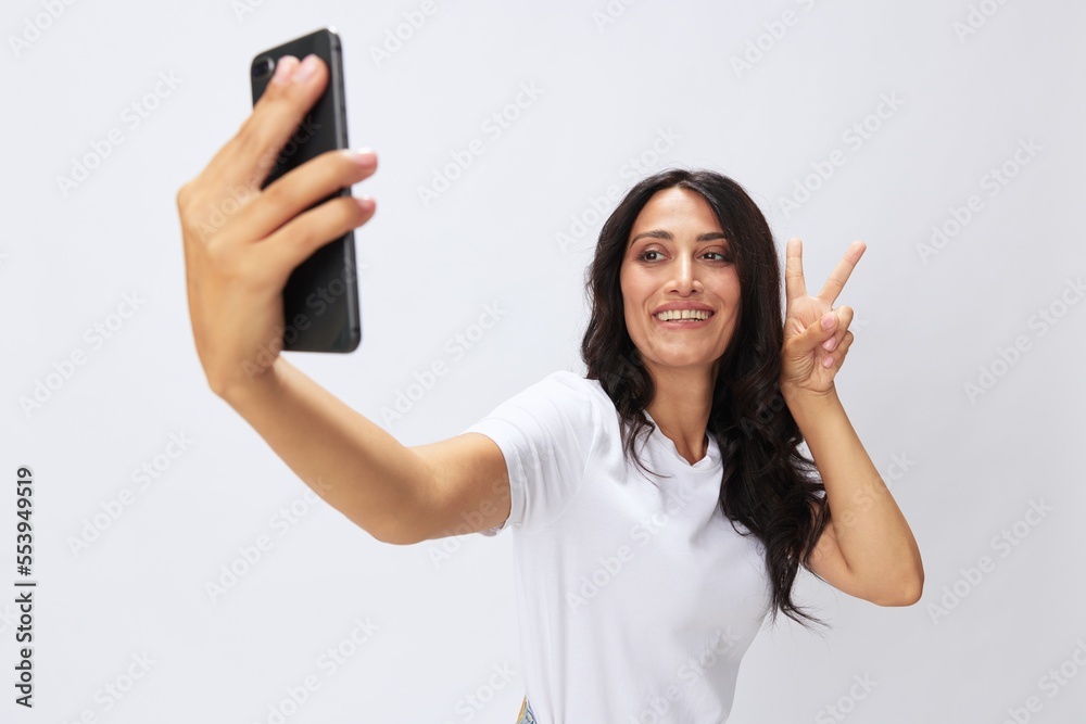 Woman blogger with a phone in her hands photo content, video call, selfie smile with teeth in a white t-shirt on a white background, copy space, emotions and gestures signals Woman blogger with a phone in her hands photo content, video call, selfie smile with teeth in a white t-shirt on a white background, copy space, emotions and gestures signals