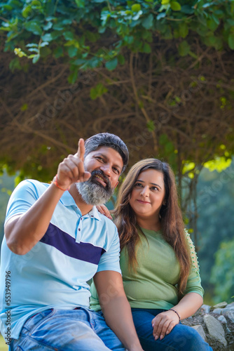 Young indian couple pointing and watching on opposite site at garden