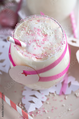 Frische leckere Milch im Glas dekoriert mit rosa Zucker, Trinkhalm, Geschenkband und Papiersternen
