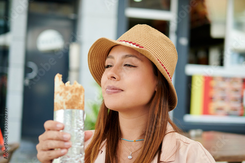 A beautiful Hispanic female in a hat eating a kebab in a cafe on a sunny day