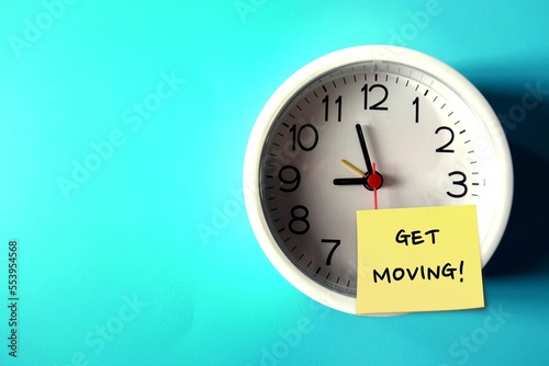 Wall clock on blue copy space background with handwritten note GET MOVING!, concept of having difficulty setting aside exercise time, reminder for health improvement by being more physically active photo