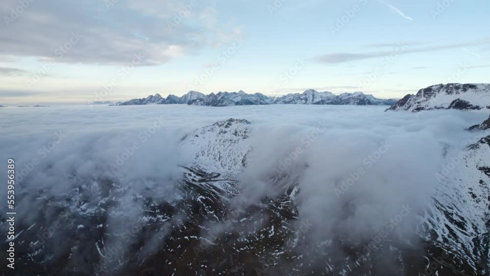 Aerial panning shot revealing a curtain of clouds falling over the snow-capped mountains of the European alps Aerial panning shot revealing a curtain of clouds falling over the snow-capped mountains of the European alps