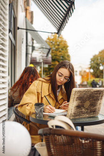 Businesswoman taking notes in planner and working on project in cafe on city street  © Dzmitry