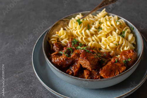 Hungarian goulash with pasta in a bowl isolated on dark table background.