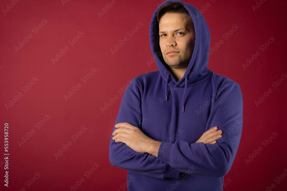 Confident young man in purple sweatshirt posing and looking at camera on red background